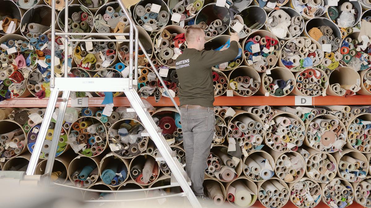 Employee selecting upholstery fabrics from a shelf of fabric rolls
